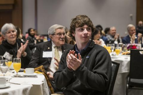 Student clapping in the foreground at a table with donors sitting behind him