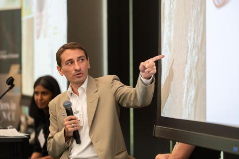 Professor James Wray holds microphone and points to powerpoint slide during his presentation
