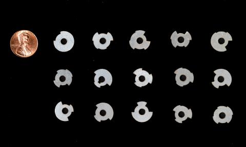 A group of 15 round metal tags of various shapes and a penny to show the tags are smaller.